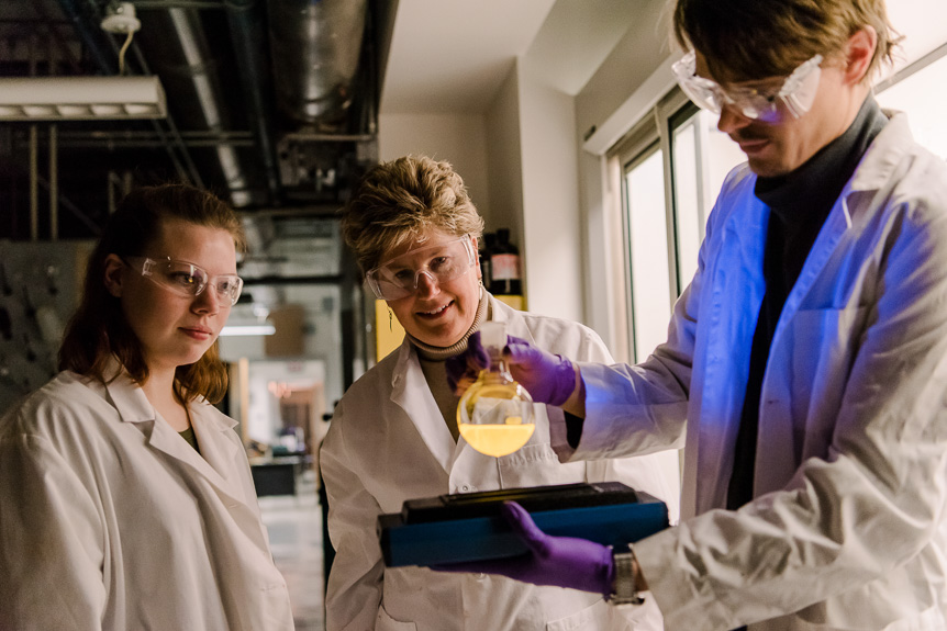 Sample image - 2 UMBC students and a faculty member evaluate liquid in a dimly lit lab